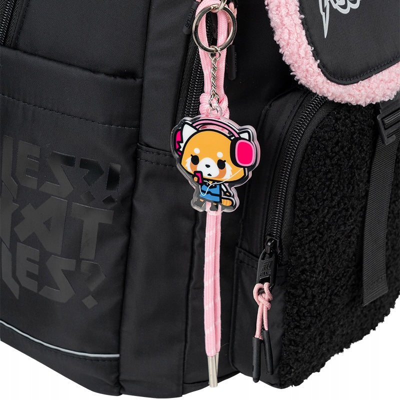 Tematyczna zawieszka z postacią Aggretsuko przy czarnym plecaku.