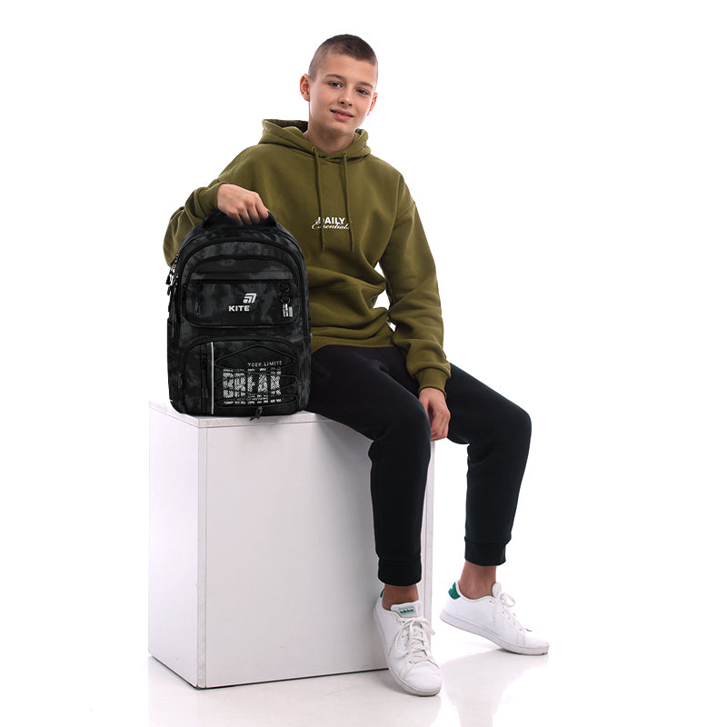 Nastolatek siedzący obok szarego plecaka Kite, co pozwala ocenić rzeczywiste wymiary i wygląd modelu.