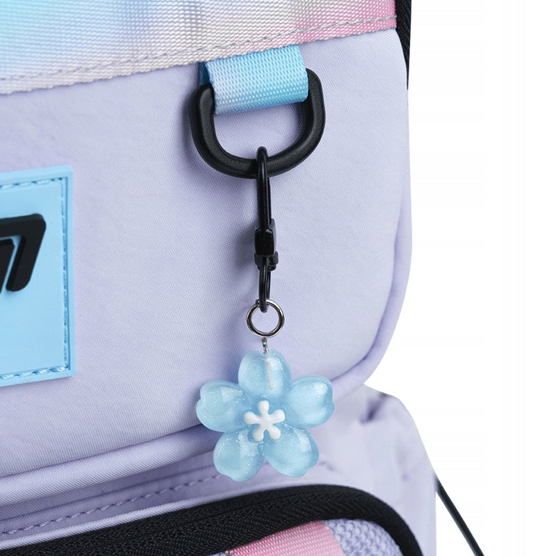 Zbliżenie na dekoracyjną podwieszkę w kształcie kwiatka, która zdobi zamek plecaka Kite.