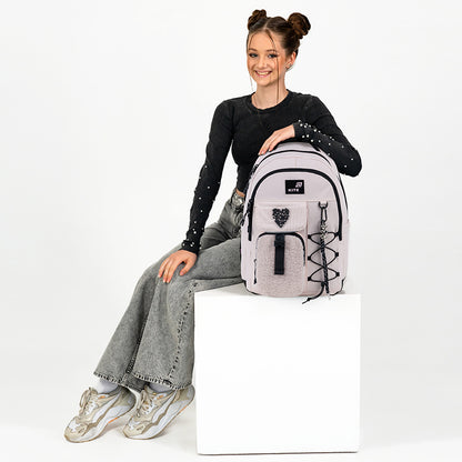 Modelka nastolatka siedząca obok jasnoróżowego plecaka Kite, co pozwala ocenić jego wielkość i styl.