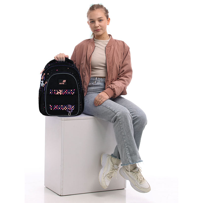 Dziewczynka siedząca obok plecaka, prezentująca jego wielkość w skali.