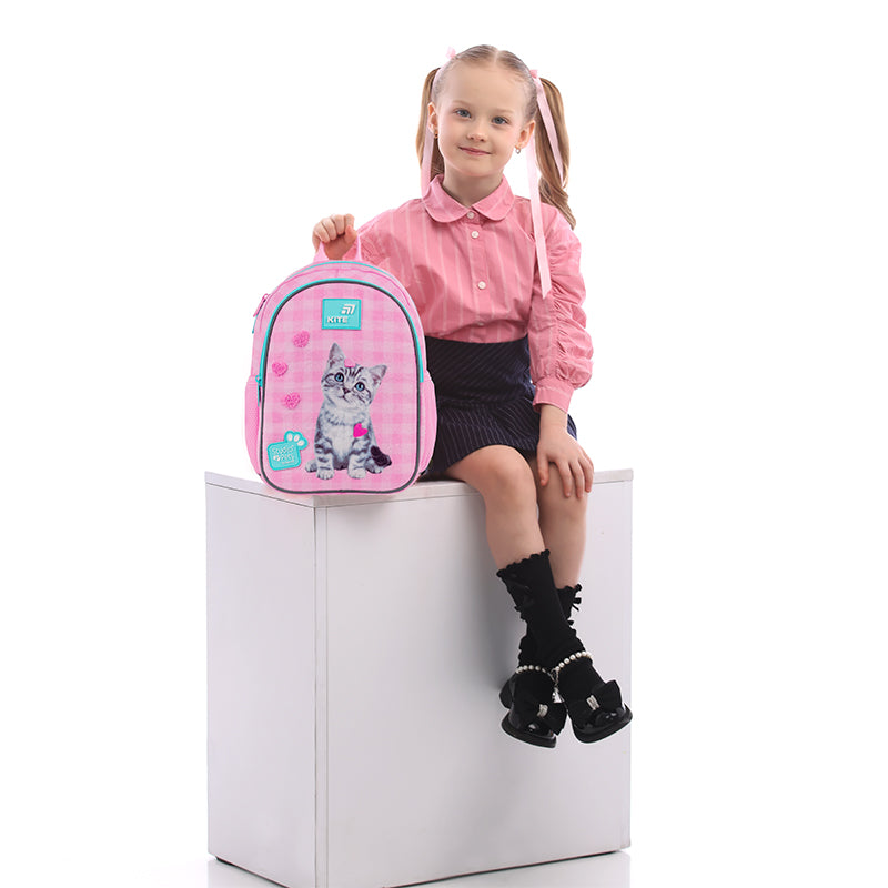 Mała modelka siedząca obok różowego plecaka z kotkiem.